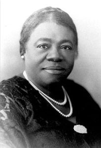 Headshot of Dr. Mary Mcleod Bethune African American women posed with hear pulled back wearing dark top with double string of white pearls. 