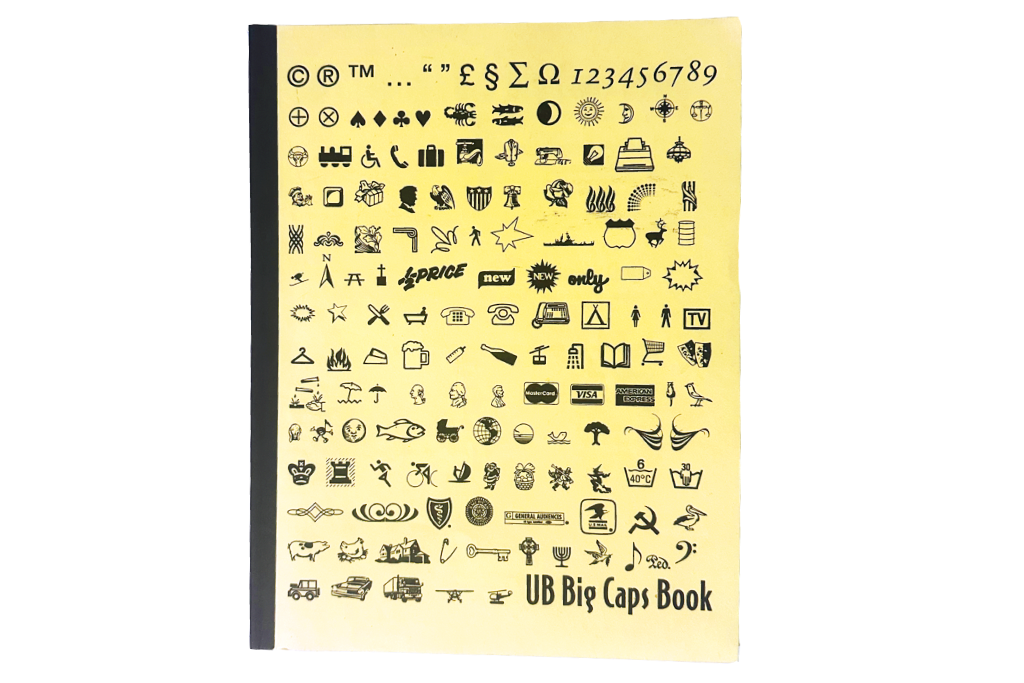 Image of a yellow book with various special characters (dingbats) showcased from top to bottom on its cover. The title “UB Big Caps Book” is placed amongst the characters in the bottom right corner, written in a condensed san serif font.